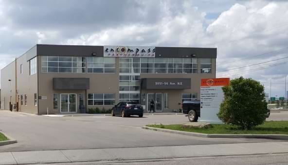 Front view of the
Encompass Partnerships building, a two-story structure with large
glass windows, located in a parking area under a partly cloudy sky.